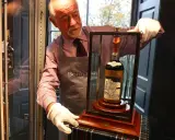 Mann mit weißen Handschuhen präsentiert eine Flasche des teuersten Weins der Welt, eine seltene Macallan 60 Year Old.