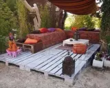 Un rincón zen con sofás y mesas bajas creados con jardineras con palets, cojines coloridos y faroles.