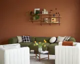 Salon cosy aux murs couleur cognac, canapé vert, fauteuils blancs et table basse.