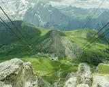 Vista mozzafiato dal passo Pordoi, con montagne innevate, verdi pendii e una strada tortuosa.