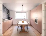 Une cuisine salle à manger et salon dans la même pièce, avec des meubles roses, un papier peint floral et une table en bois.
