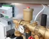 Detalle de tuberías de latón con manómetro y una válvula de seguridad. En el fondo, un panel de control.