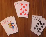 Karty na drewnianym stole: as, dwójka, joker i inne. Joker w kartach wygląda jak wesoły błazen.