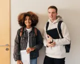 Dwóch studentów, dziewczyna z kręconymi włosami i chłopak, przygotowuje się do nauki. Może właśnie szukają informacji, jak napisać artykuł po angielsku.