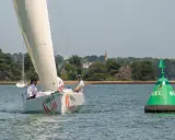 Voile blanche sur l'eau, le voilier "Bihan 6.50" navigue avec deux personnes à bord. Une bouée verte marque le passage.