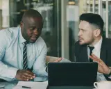 Deux hommes d'affaires discutent d'une nouvelle démarche, synonyme de succès. Ils sont concentrés sur une tablette.