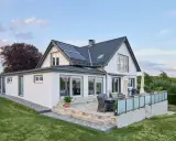 Modernes Haus mit Anbau und Terrasse. Die Solaranlage auf dem Dach deutet auf niedrige Energiekosten hin.