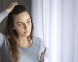 Zamyślona dziewczyna, jakby napalona sąsiadka, patrzy przez okno.