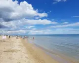 Una giornata di sole sulla spiaggia del cuore Riccione, con bambini che giocano e adulti che si godono il mare calmo sotto un cielo azzurro e nuvoloso.