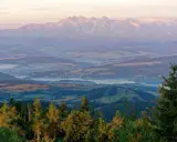 Widok na Tatry o wschodzie słońca. Mgły unoszą się nad doliną, a lasy i pola tworzą malowniczy krajobraz. W oddali widać **gorc** szczytów.