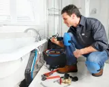 Plombier vérifiant la pose de la baignoire, outils et tuyaux à proximité.