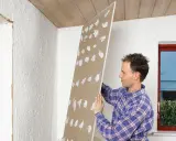 Man håller upp en gipsskiva med spackelklumpar, redo att måla direkt på gips.