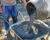 Robotnik wylewa świeży beton B25 z betoniarki do taczki. Sprawdzamy beton b25 cena za m3.