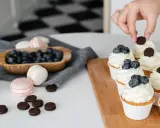 Des cupcakes décorés avec une crème chiboust aérienne, des myrtilles et des biscuits. Des macarons et des myrtilles sont disposés à côté.