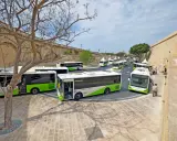 Malta autobusy z lotniska czekają na pasażerów. Wiele zielono-białych pojazdów stoi w rzędzie przy zabytkowych murach.