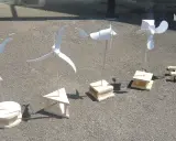 Cinq maquettes éoliennes, fabrication simple en bois, alignées sur un sol gris.