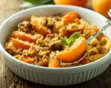 Ein köstlicher Aprikosen Crumble in einer weißen Schale, garniert mit Minze. Perfekt für einen süßen Genuss.