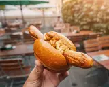Eine Hand hält eine Bratwurst im Brötchen mit Senf. Ein leckerer Snack, aber die Bratwurst Kalorien sollte man im Auge behalten.
