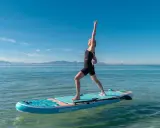 Kvinna utövar sup yoga på en paddleboard i lugnt vatten med berg i bakgrunden.