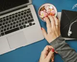 Eine Hand greift nach Süßigkeiten neben einem Laptop. Das Bild symbolisiert assoziatives Lernen: Belohnung und Fokus.