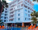 Biały hotel z balkonami i basenem, otoczony palmami. Idealne miejsce na fafa mel holiday.