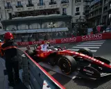 Lewis Hamilton im Ferrari-Boliden rast durch Monaco. Zuschauer säumen die Strecke, die Casino-Werbung blinkt.