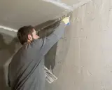 Hombre aplicando masilla en una esquina para quitar el gotele del techo.