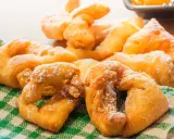 Beignets dorés saupoudrés de sucre glace sur un torchon à carreaux verts.