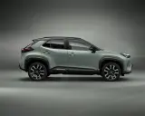 Nowy, zielony toyota crossover Yaris Cross z czarnym dachem i felgami stoi na szarym tle.