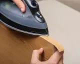 Persona aplica cinta de cantear a un borde de madera con una plancha.