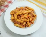 Plato de macarrones con carne picada y salsa de tomate, decorado con un paño a cuadros y espaguetis secos al fondo.