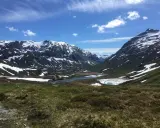 Vacker dalgång med snöklädda berg, en sjö och grönskande sluttningar. En väg slingrar sig fram, kanske en del av trollväggen.