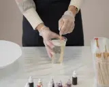 Hände mit Handschuhen mischen zwei komponenten harz in einem Becher. Kleine Farbtropfflaschen stehen bereit.