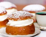Semlor, en fest vid fastan, pudrade med florsocker och fyllda med grädde. En kopp kaffe i bakgrunden.