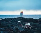 En fyr lyser över klippor och röda hus vid havet. En idyllisk plats för unika hotell Sverige.