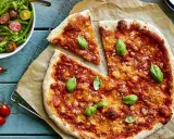 En härlig hemmagjord pizza med tomatsås och ost, toppad med färsk basilika. Bredvid en fräsch sallad med gröna bönor och körsbärstomater.