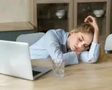 Zmęczona kobieta śpi na biurku obok laptopa. Objawy wypalenia zawodowego, czas na L4.
