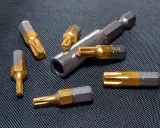 Różne rodzaje bitów Torx, w tym T25 i T40, leżą obok metalowego uchwytu na czarnym, teksturowanym tle.