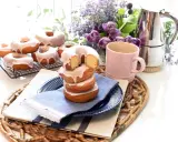 Deliciosos donuts caseros glaseados, apilados en un plato con una taza rosa y flores moradas.