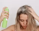 Frau sprüht sich Haarspray auf die Kopfhaut, was die Haare austrocknen kann.