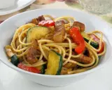 Un plato de espaguetis con pimientos rojos y calabacín salteados, con trozos de carne.