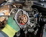 Main d'un mécanicien tenant une pompe à eau électrique démontée, prête pour la réparation. Le moteur est visible en arrière-plan.
