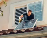 Instalación de placas solares en comunidad de vecinos. Un hombre con guantes y gafas de seguridad coloca un panel solar en un tejado.