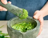 Frisches basilikum pesto wird in einem Mörser zerstoßen. Tropfen des grünen Pesto fallen vom Stößel in die Schüssel.