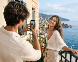 Un homme prend une photo de sa compagne sur un balcon avec vue sur la mer. Une petite attention pour immortaliser leur bonheur.