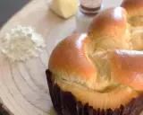 Un pan brioche dorado y esponjoso, listo para ser disfrutado. A su lado, ingredientes para su elaboración: harina, mantequilla y sal.