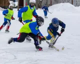 Barn i full fart med hockeyklubbor och hjälmar, ivriga att vinna pucken. De har roligt med lekar på isen.