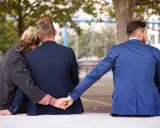 Trójkąt miłosny. Dwoje ludzi siedzi blisko siebie, a trzeci mężczyzna dyskretnie trzyma ich za rękę. To pokazuje, dlaczego zdrada emocjonalna tak boli.