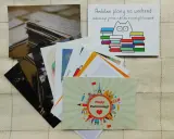 Stos pocztówek, jedna z kotem i książkami, druga z zabytkami świata. Tak wygląda pocztówka wysłana z podróży.