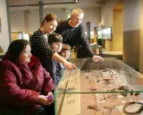 A family, including a woman in a wheelchair, examines artifacts in a museum display, perhaps inspired by famous art curators.
